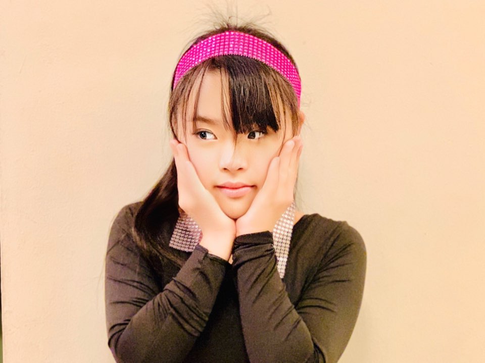 Megan Tang in a pink headband, posing with her hands on her cheeks