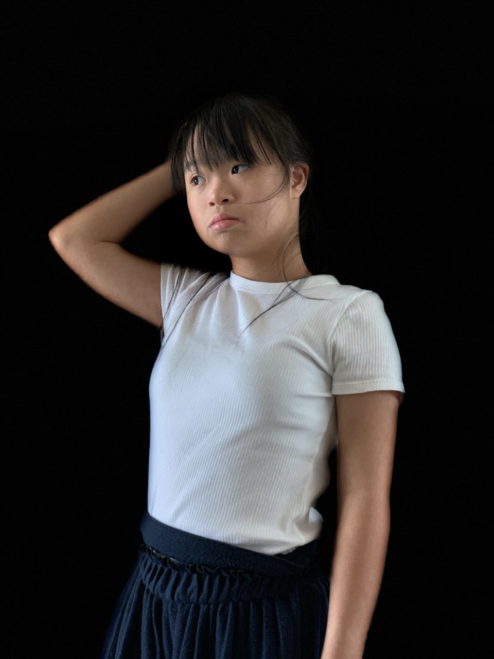 Megan Tang in a white T-shirt against a black backdrop, one hand behind her head